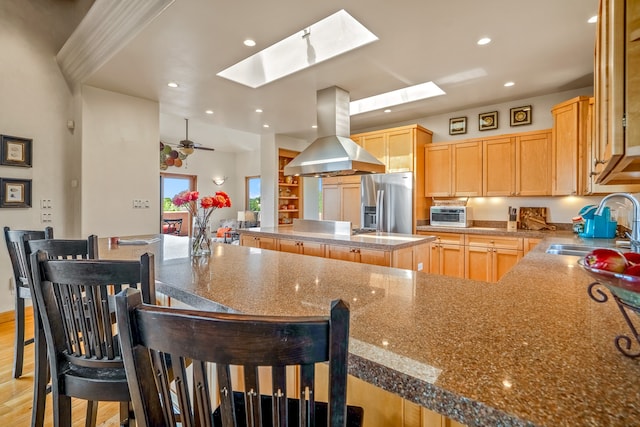 kitchen featuring light hardwood / wood-style flooring, ceiling fan, stainless steel fridge with ice dispenser, island exhaust hood, and a skylight