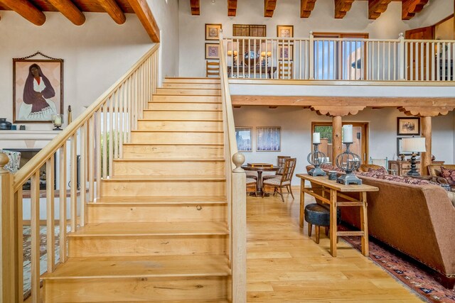 staircase with beam ceiling, a high ceiling, and hardwood / wood-style flooring