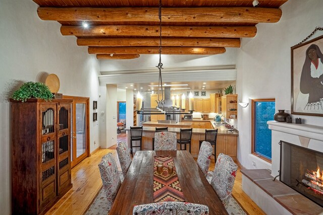 dining room featuring beamed ceiling, light hardwood / wood-style flooring, a fireplace, and wooden ceiling