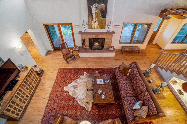 living room featuring a tiled fireplace, light wood-type flooring, and a towering ceiling