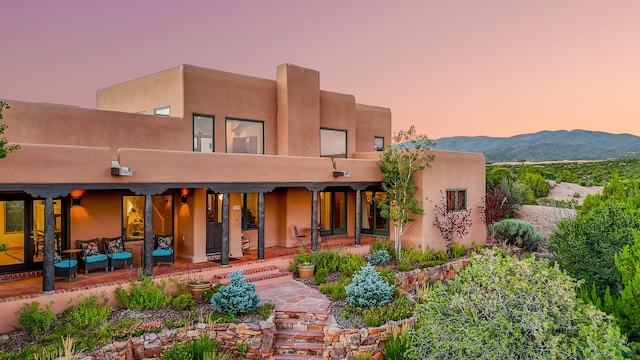 back house at dusk with a mountain view and a patio area