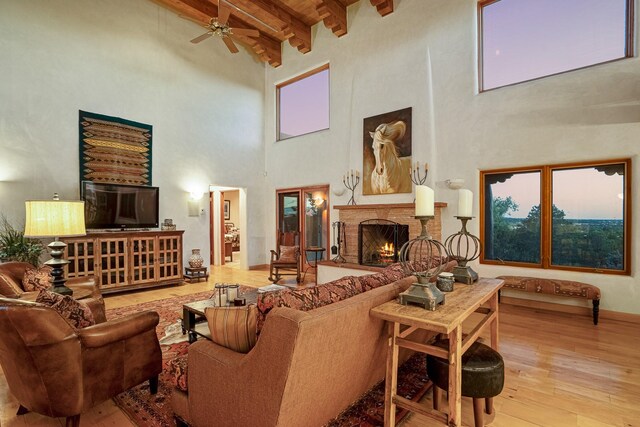 living room featuring beam ceiling, light hardwood / wood-style flooring, a brick fireplace, and a high ceiling