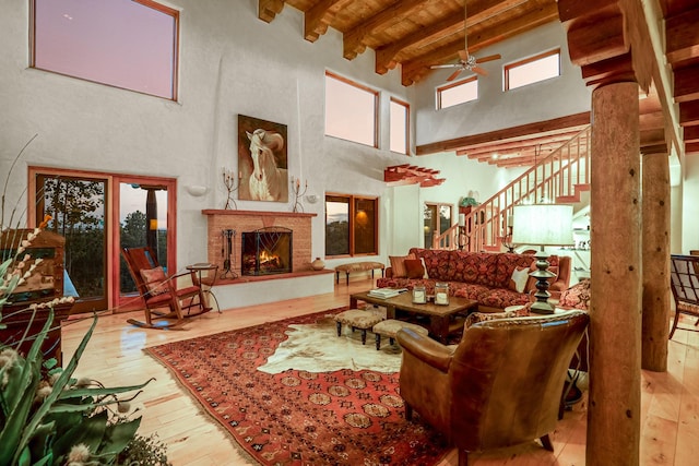 living room with ceiling fan, a towering ceiling, beam ceiling, hardwood / wood-style flooring, and decorative columns