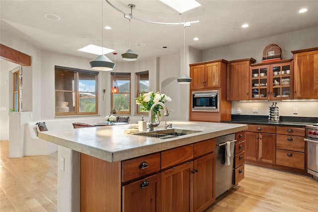 kitchen featuring stainless steel appliances, hanging light fixtures, light wood-type flooring, an island with sink, and sink