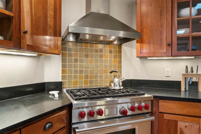 kitchen featuring designer range, decorative backsplash, wall chimney range hood, and dark stone countertops