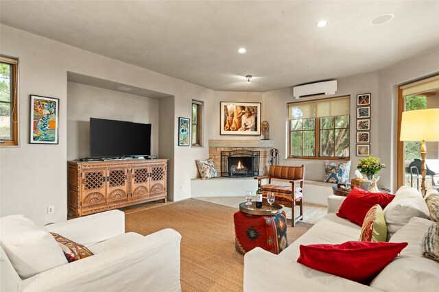 living room featuring a wall unit AC, a stone fireplace, light wood-type flooring, and a healthy amount of sunlight