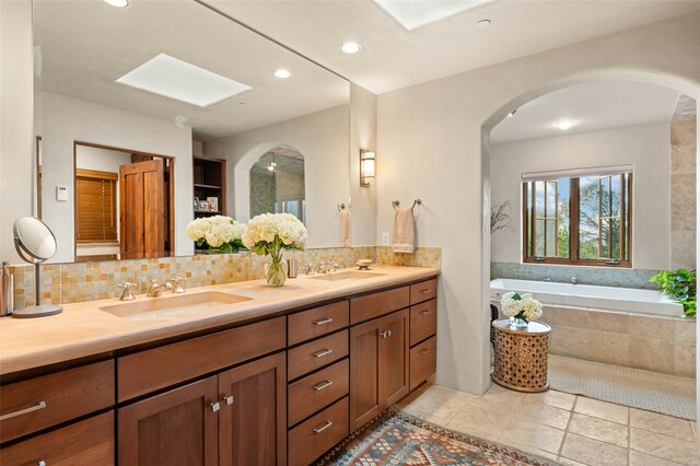 bathroom with dual bowl vanity, tasteful backsplash, tiled tub, and tile patterned flooring