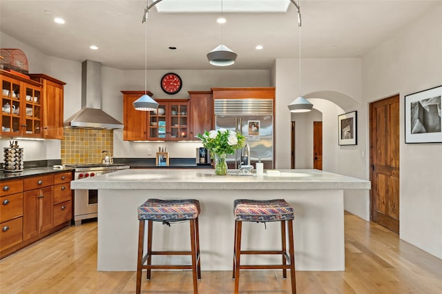 kitchen with light wood-type flooring, decorative backsplash, wall chimney range hood, and premium appliances