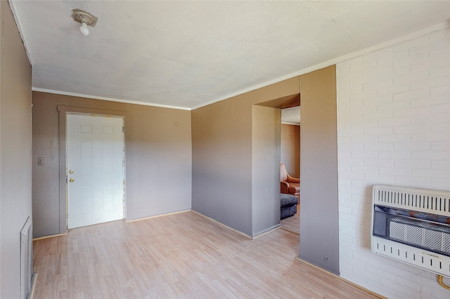 empty room with crown molding, heating unit, and light hardwood / wood-style floors