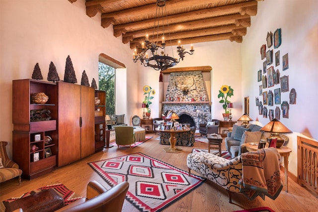 living room featuring a towering ceiling, a fireplace, light hardwood / wood-style flooring, beamed ceiling, and a chandelier