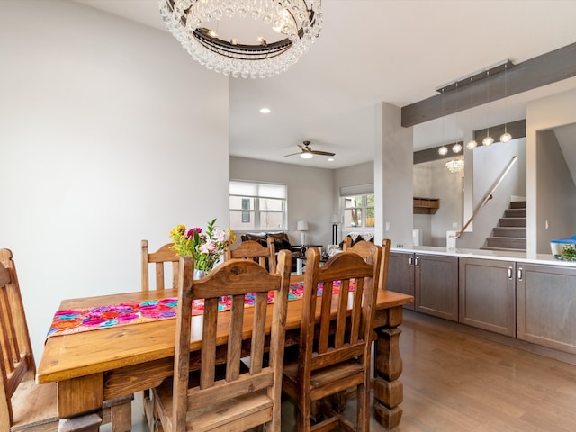 dining space with ceiling fan with notable chandelier and light hardwood / wood-style floors