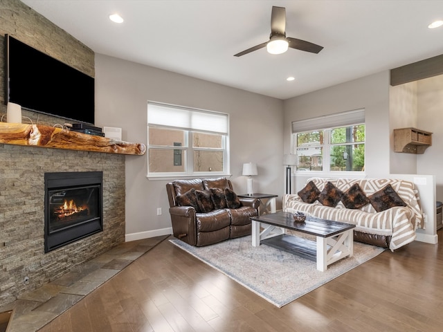 living room featuring ceiling fan, dark hardwood / wood-style flooring, and a stone fireplace