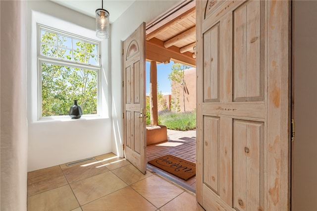 doorway to outside with wood ceiling, beamed ceiling, light tile patterned floors, and a healthy amount of sunlight