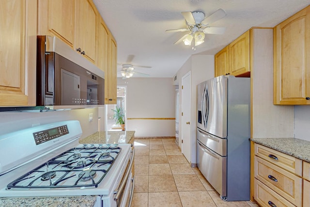 kitchen featuring ceiling fan, light brown cabinets, light tile patterned flooring, light stone counters, and stainless steel appliances