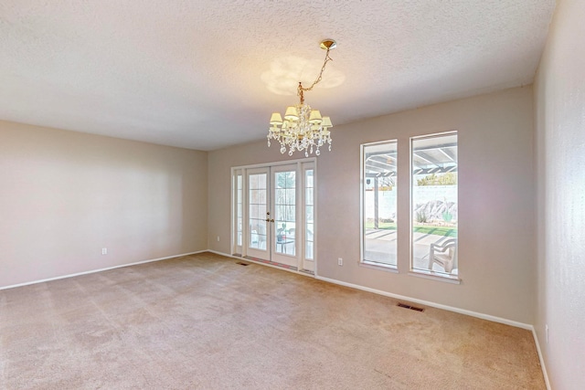 unfurnished room with a textured ceiling, light colored carpet, and a notable chandelier