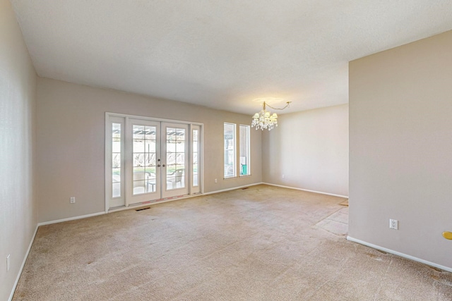 empty room with light carpet, a chandelier, a textured ceiling, and french doors