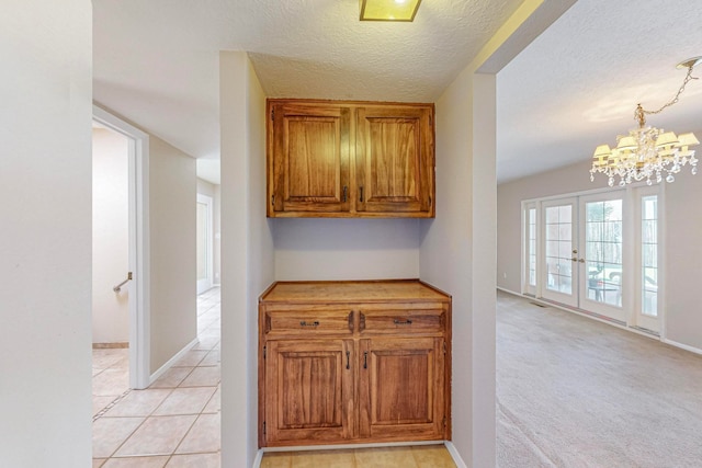 kitchen with pendant lighting, french doors, a textured ceiling, light carpet, and a notable chandelier