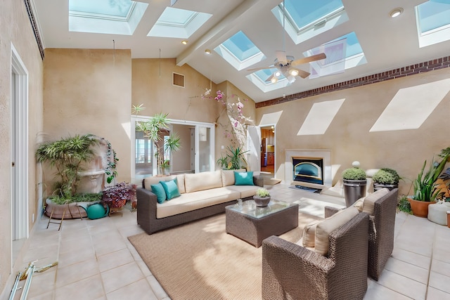 living room featuring ceiling fan, beamed ceiling, a skylight, light tile patterned floors, and high vaulted ceiling