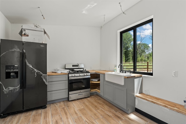 kitchen with gray cabinetry, light wood-type flooring, black fridge with ice dispenser, and gas range oven