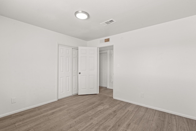 unfurnished bedroom with a closet, baseboards, visible vents, and wood finished floors