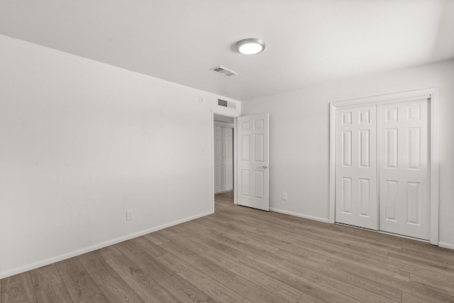 unfurnished bedroom with visible vents, a closet, baseboards, and wood finished floors