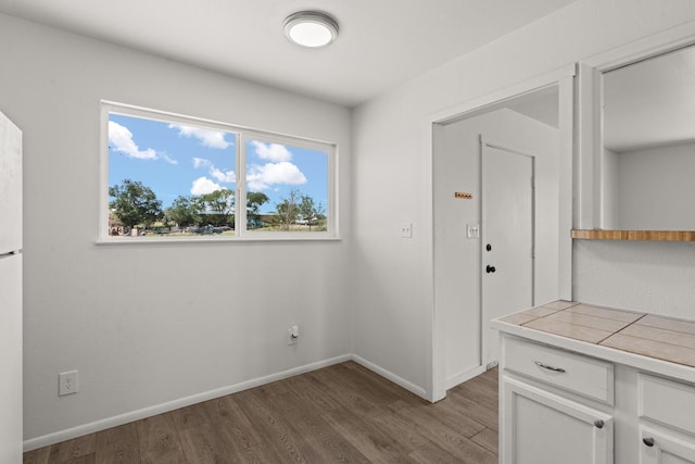 kitchen with tile counters, baseboards, white cabinets, and wood finished floors