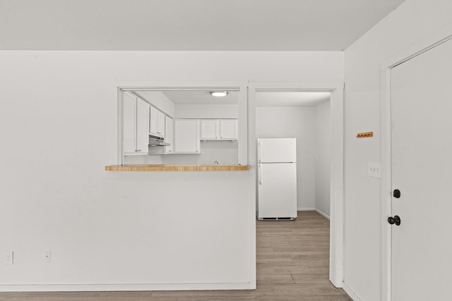 kitchen featuring freestanding refrigerator, white cabinetry, a peninsula, under cabinet range hood, and light wood-style floors