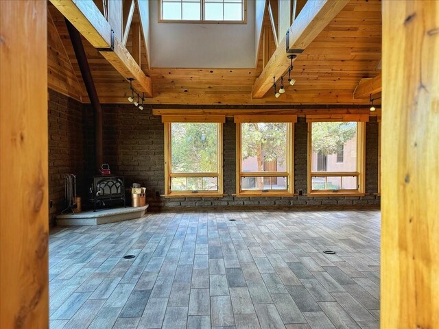 125 Tierra Del Dios, Rowe, NM 87562 - unfurnished living room featuring beamed ceiling, high vaulted ceiling, a wood stove, and wood finished floors