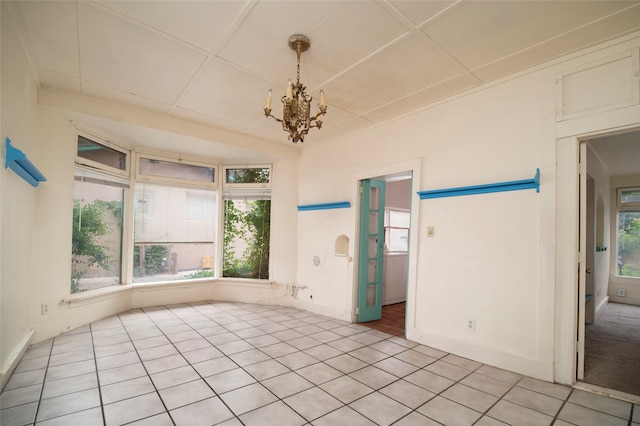 empty room with a wealth of natural light, light tile patterned floors, and an inviting chandelier