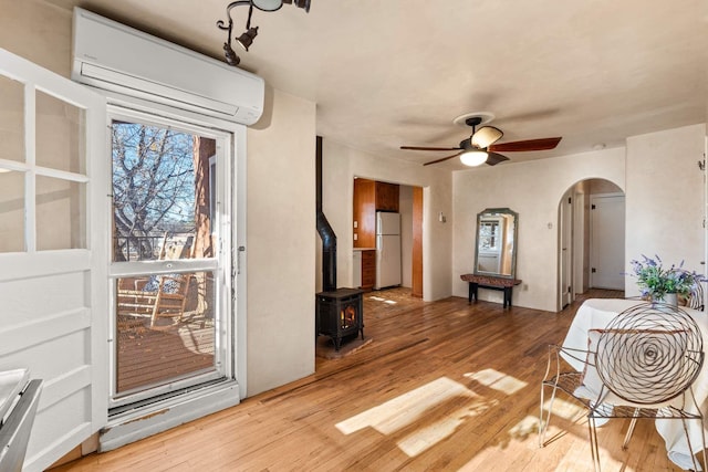 interior space featuring ceiling fan, a wood stove, a wall unit AC, and light hardwood / wood-style flooring