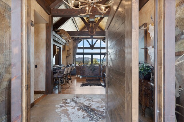 interior space with a chandelier, wood walls, a towering ceiling, beam ceiling, and hardwood / wood-style flooring