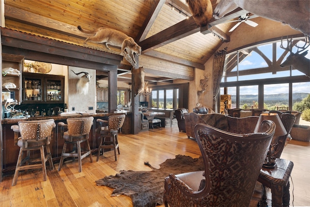 dining area with beam ceiling, light wood-style floors, a ceiling fan, wood ceiling, and bar