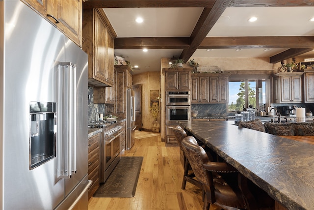 kitchen with light wood finished floors, high end appliances, dark countertops, decorative backsplash, and beamed ceiling