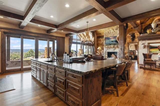 kitchen with beam ceiling, dark brown cabinets, sink, light wood-type flooring, and a stone fireplace