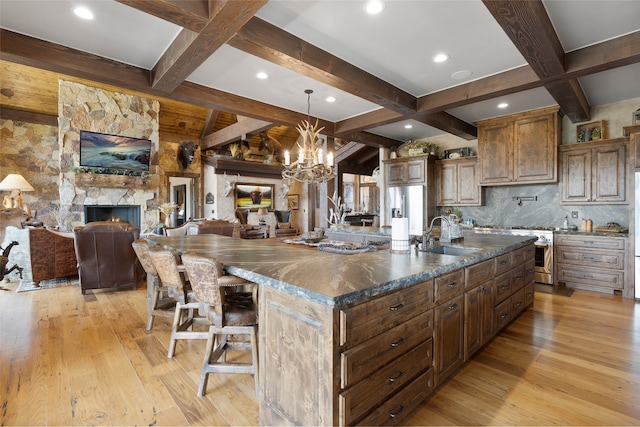 kitchen with a stone fireplace, beam ceiling, a large island, light hardwood / wood-style floors, and sink