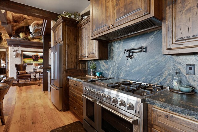 kitchen with high end appliances, dark stone countertops, light wood-type flooring, and dark brown cabinetry