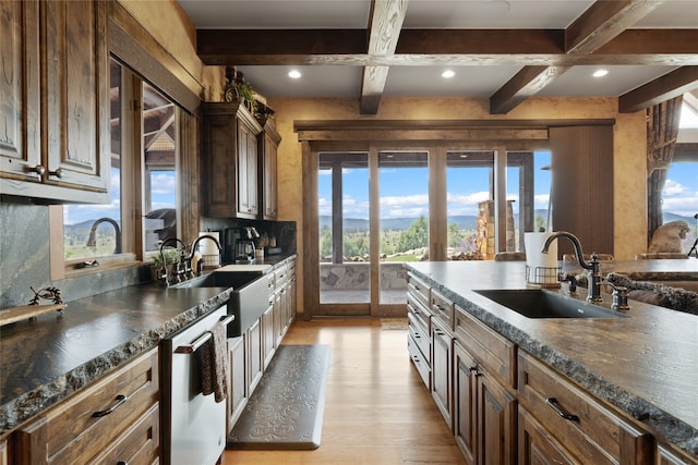 kitchen with stainless steel dishwasher, dark countertops, a sink, and beamed ceiling