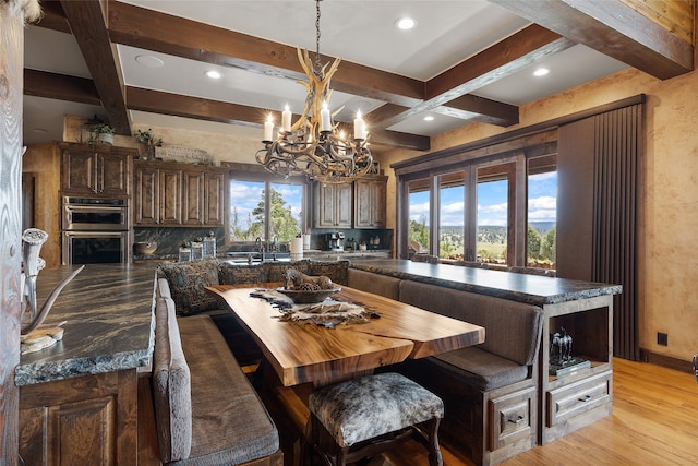 kitchen featuring beam ceiling, backsplash, light wood-style floors, stainless steel double oven, and a kitchen island