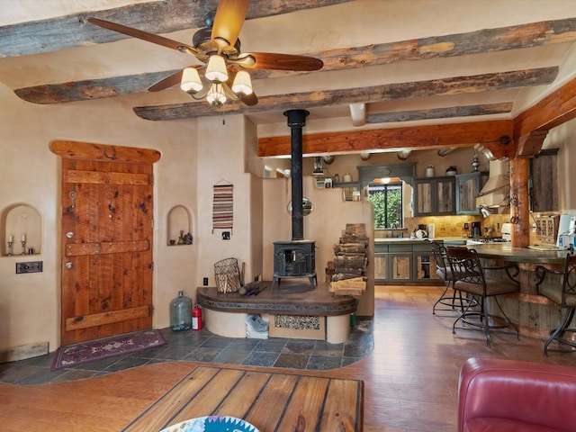 living room with beamed ceiling, a wood stove, a ceiling fan, and hardwood / wood-style floors