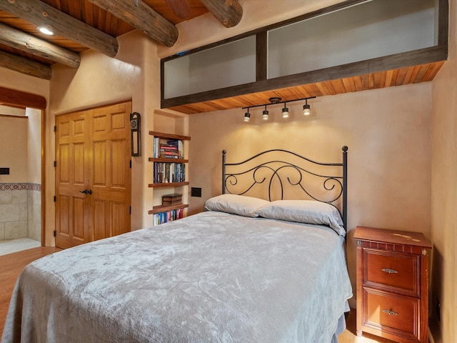 bedroom featuring beamed ceiling, ensuite bath, wooden ceiling, and track lighting