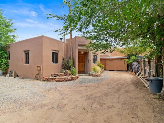 pueblo revival-style home with stucco siding, driveway, and fence