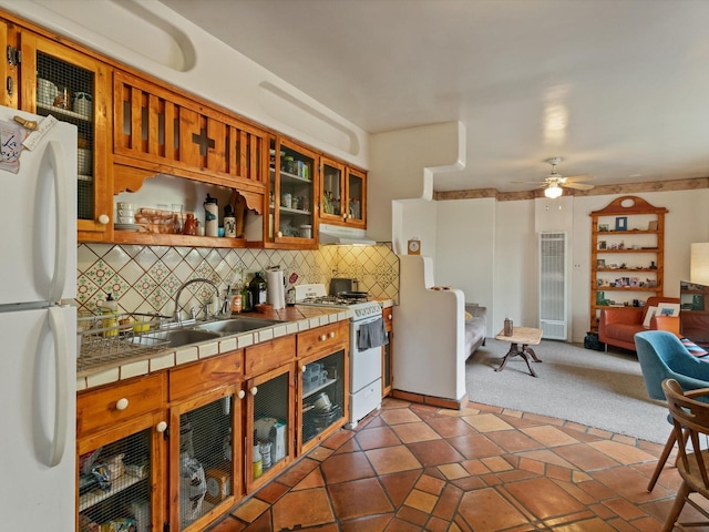 kitchen featuring white appliances, tile countertops, a sink, under cabinet range hood, and tasteful backsplash