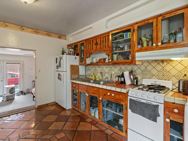 kitchen with tile counters, under cabinet range hood, decorative backsplash, white appliances, and a sink