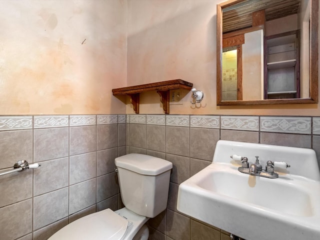 half bathroom featuring tile walls, toilet, wainscoting, and a sink