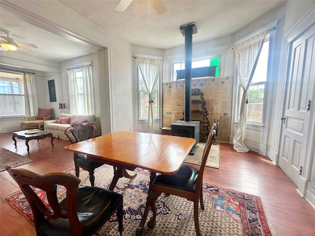 dining room featuring ceiling fan, hardwood / wood-style floors, a wood stove, and a textured ceiling