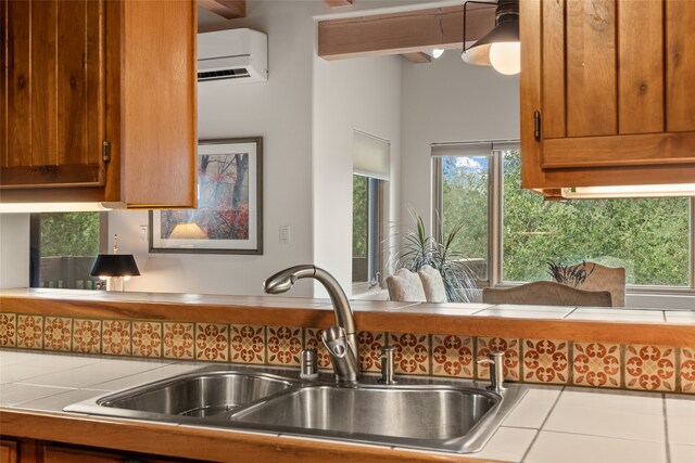 kitchen featuring a wall mounted air conditioner, a sink, tile counters, and brown cabinets