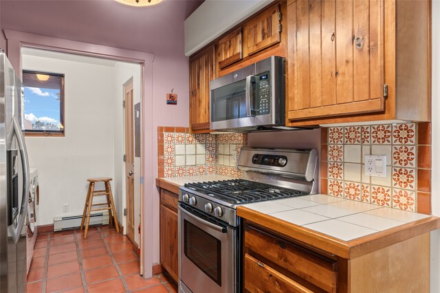 kitchen with tile countertops, a baseboard radiator, appliances with stainless steel finishes, and brown cabinets