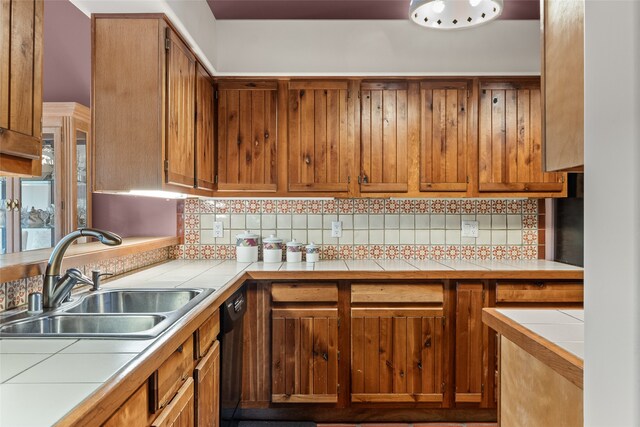 kitchen featuring brown cabinets, a sink, tile countertops, and decorative backsplash