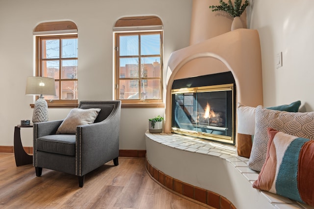 living area with baseboards, wood finished floors, and a glass covered fireplace