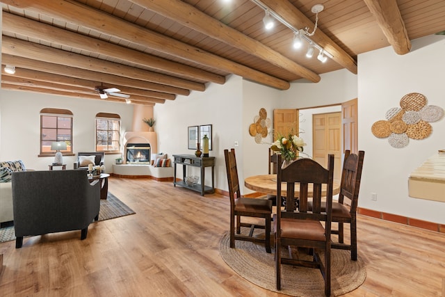 dining area with light wood-style flooring, wood ceiling, beam ceiling, a glass covered fireplace, and track lighting